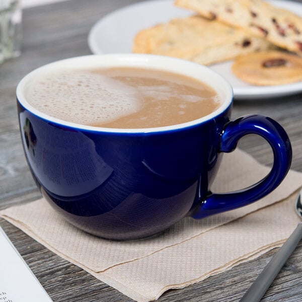 A Tuxton cobalt blue cappuccino cup filled with coffee on a table with cookies.