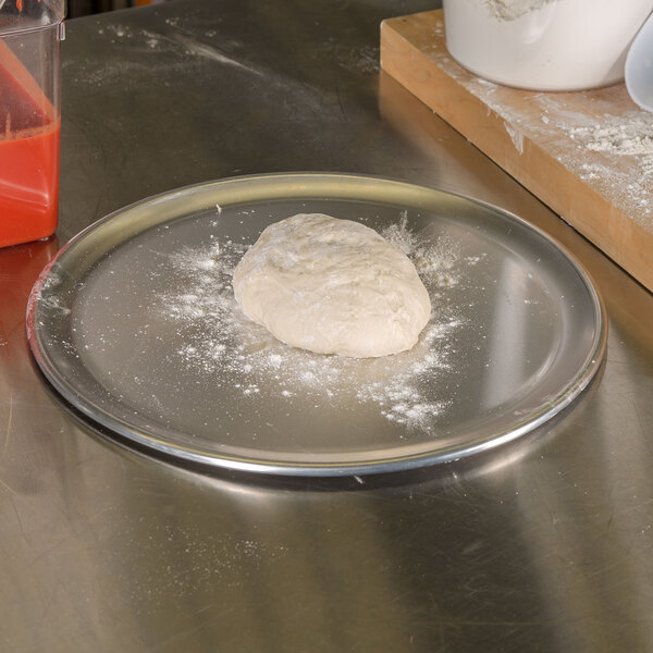 A ball of pizza dough on an American Metalcraft aluminum pizza pan on a table.