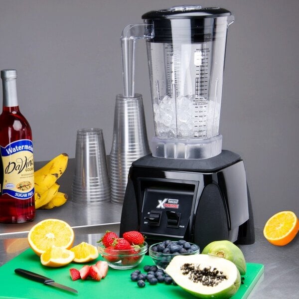 A Waring commercial blender filled with strawberries, blueberries, bananas, and papaya