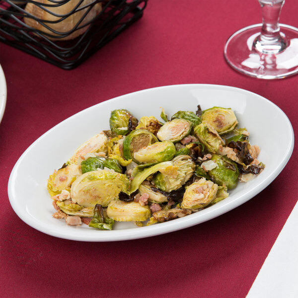 A Tuxton bright white china platter with brussels sprouts and bacon on a table.