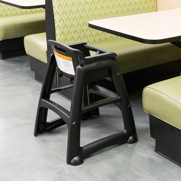 A black Rubbermaid high chair next to a table in a restaurant.