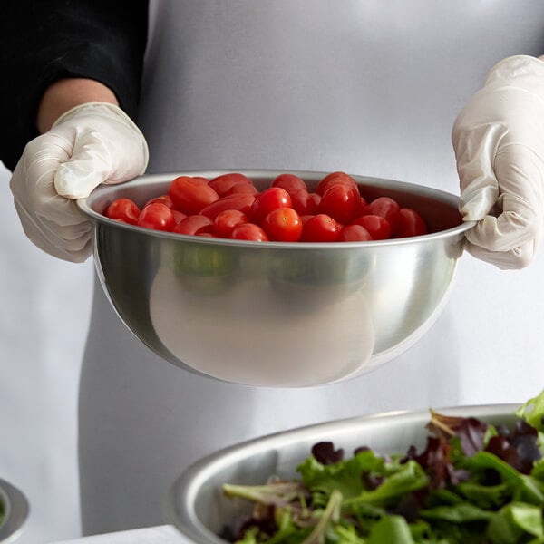 A person in gloves holding a Vollrath stainless steel mixing bowl of cherry tomatoes.