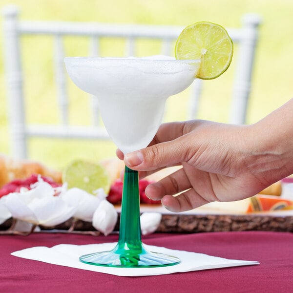 A hand holding a Fineline Flairware plastic margarita with a green base and lime wedge.