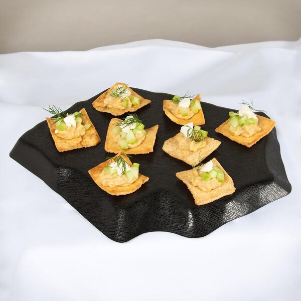 A GET Stone-Mel display tray with crackers, tortillas, and bread with cucumber and cream cheese on a table.