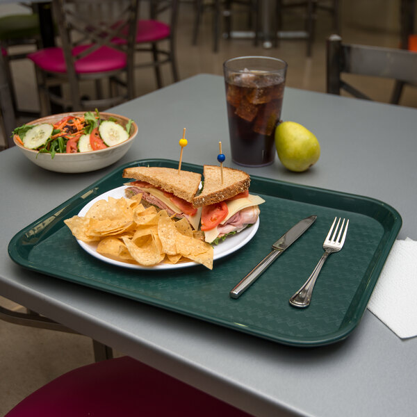 A forest green Carlisle fast food tray with a sandwich and chips on it.