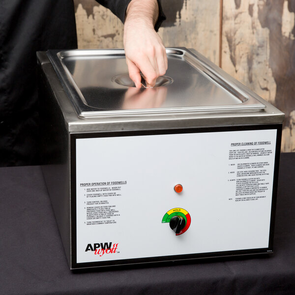 A person using an APW Wyott countertop food warmer to heat food.