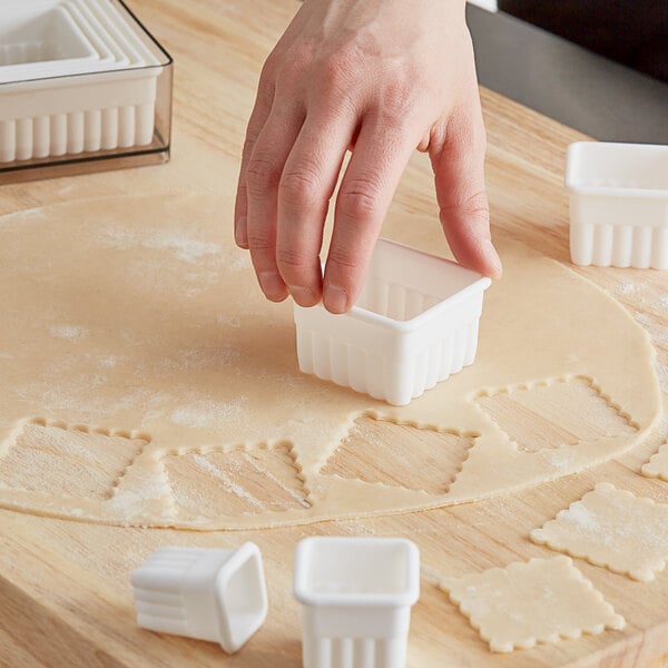 A person using Ateco fluted square pastry cutters to cut dough into small squares.