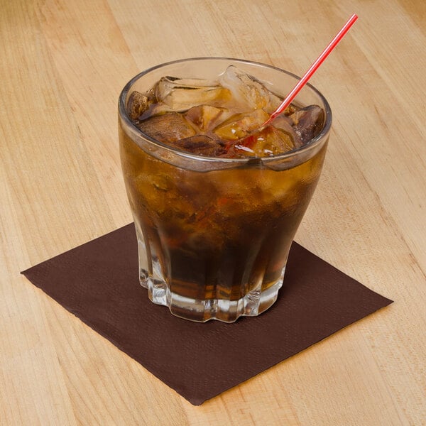 A glass with a straw and brown liquid with a brown Hoffmaster cocktail napkin.