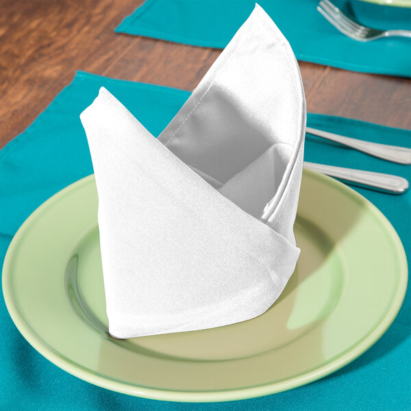 A folded white Intedge cloth napkin on a plate with silverware.