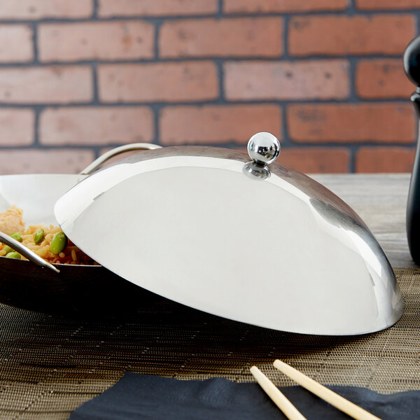A wok with a stainless steel lid on a table.