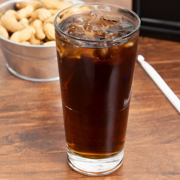 A Libbey stackable cooler glass filled with brown liquid and ice next to a bowl of peanuts.