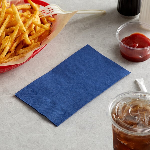 A basket of french fries and a navy blue napkin next to a drink.