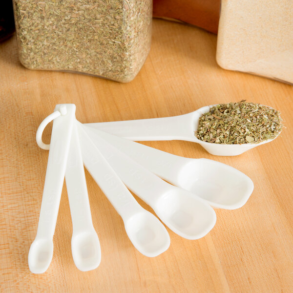 A group of white Rubbermaid plastic measuring spoons with herbs in them.