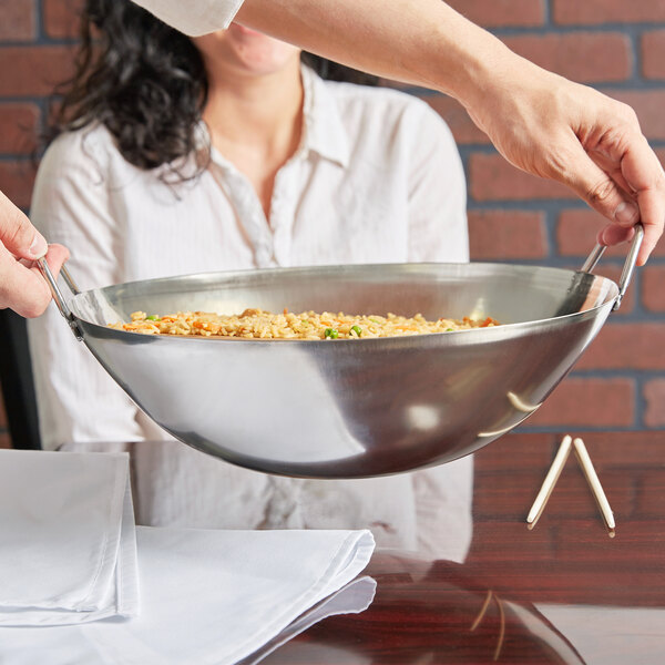 A woman holding a Town stainless steel wok serving dish filled with rice and vegetables.