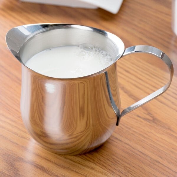 A Tablecraft stainless steel bell creamer full of milk with a handle.