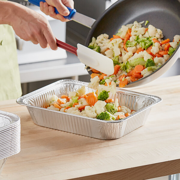 A person cooking vegetables in a Choice foil steam table pan.