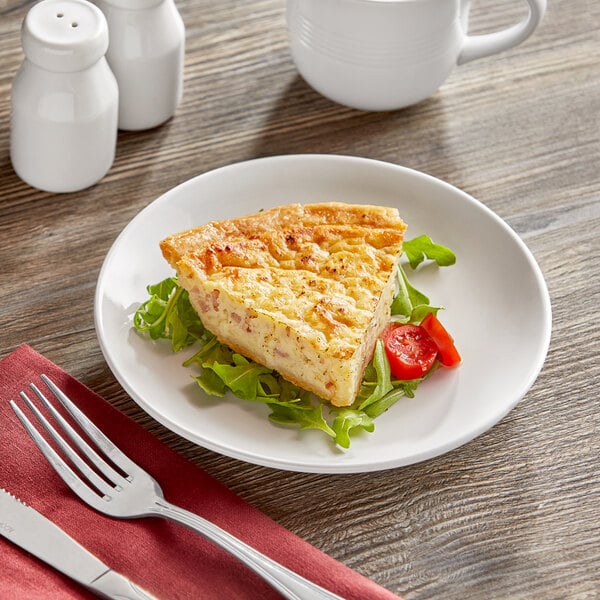 A plate with a slice of quiche and a fork on a table.