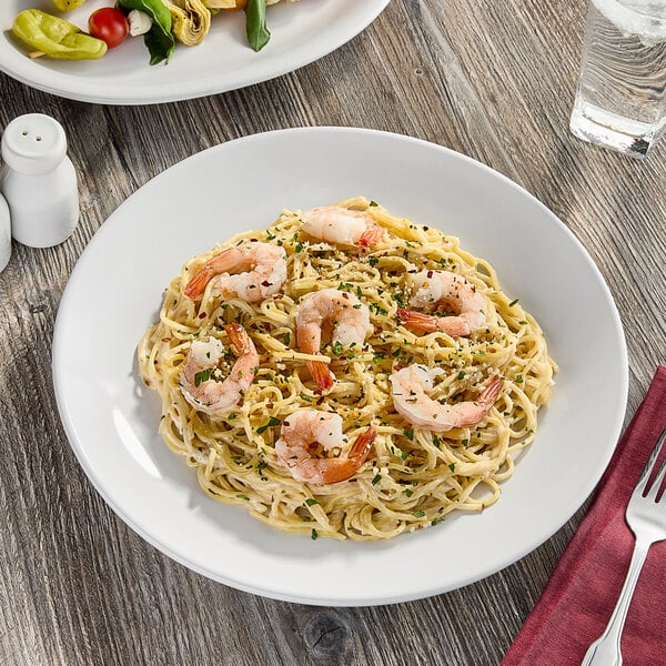A plate of pasta with shrimp and vegetables on a white Acopa stoneware plate.