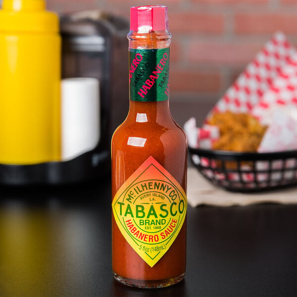 A yellow bottle of TABASCO® Habanero Hot Sauce on a table next to a roll of paper towels.