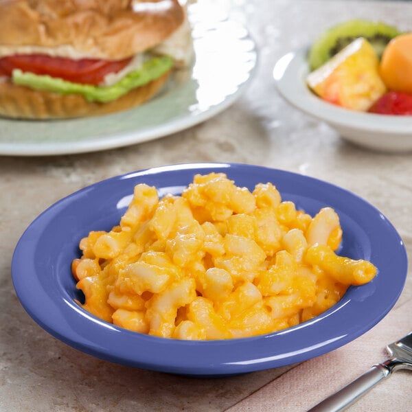 A bowl of macaroni and cheese on a table with a sandwich and an orange.