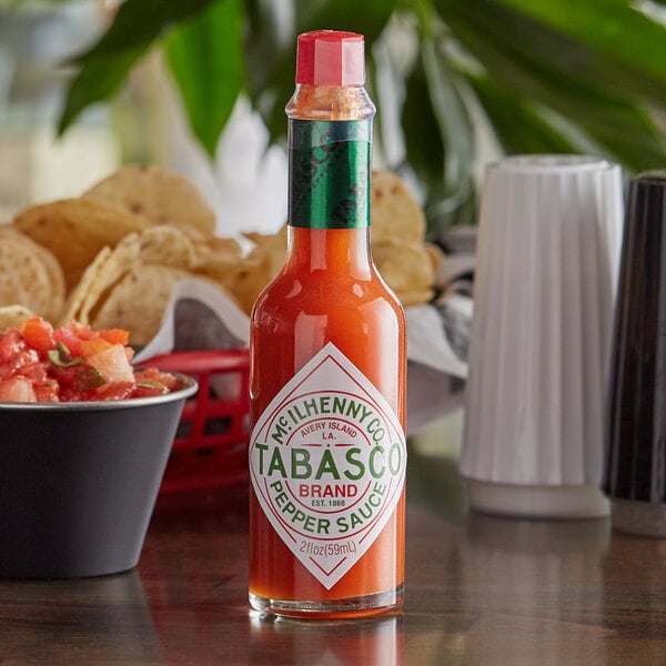 A close up of a bottle of TABASCO Original Hot Sauce next to a bowl of salsa on a table.