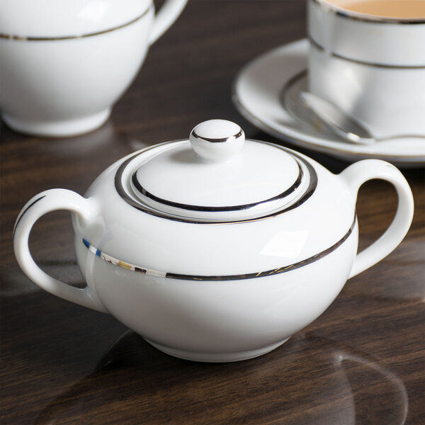 A white porcelain sugar bowl with silver double line trim and a lid.