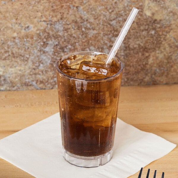 A Cambro clear plastic tumbler with brown liquid, ice, and a straw on a table.