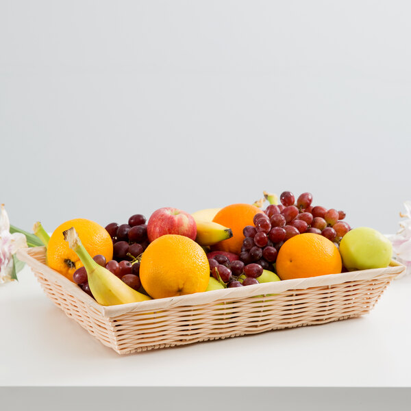 A Tablecraft rectangular woven rattan-like basket filled with fruit on a table.