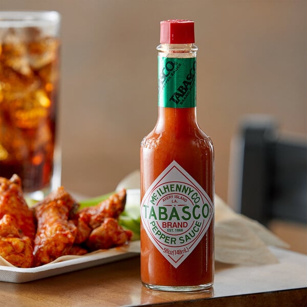 A bottle of TABASCO Original Hot Sauce on a table with chicken wings.