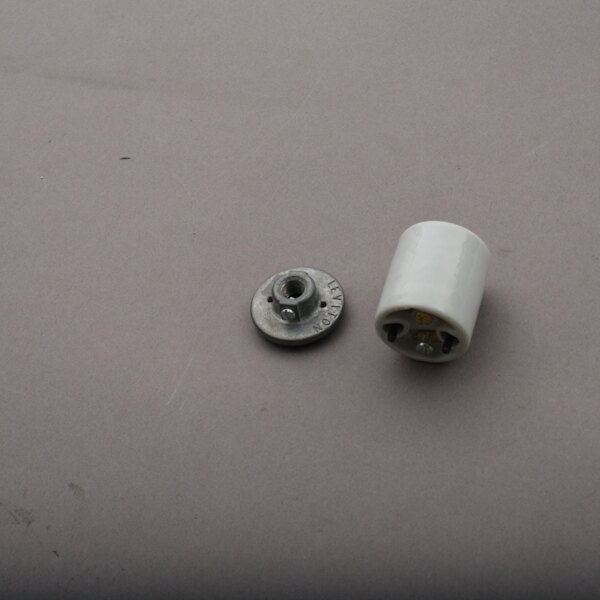 A white cylindrical object with a round metal screw on a gray surface.