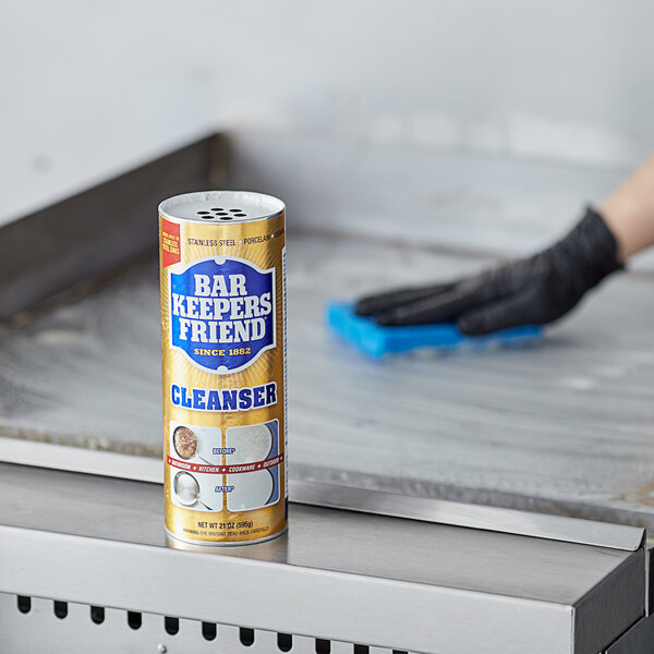 A person cleaning a grill with Bar Keepers Friend All Purpose Cleaning Powder on a counter.