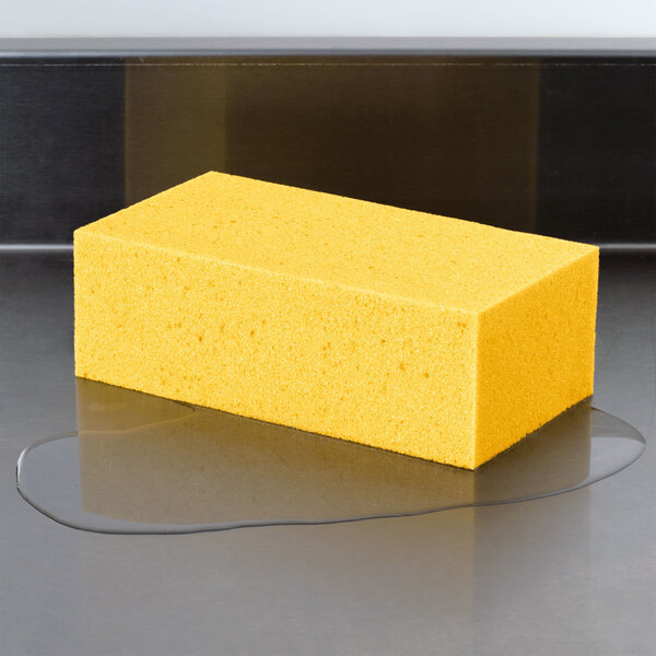 A yellow rectangular Carlisle sponge on a reflective surface.