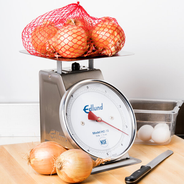 An Edlund heavy-duty portion scale on a counter with onions in a red net.