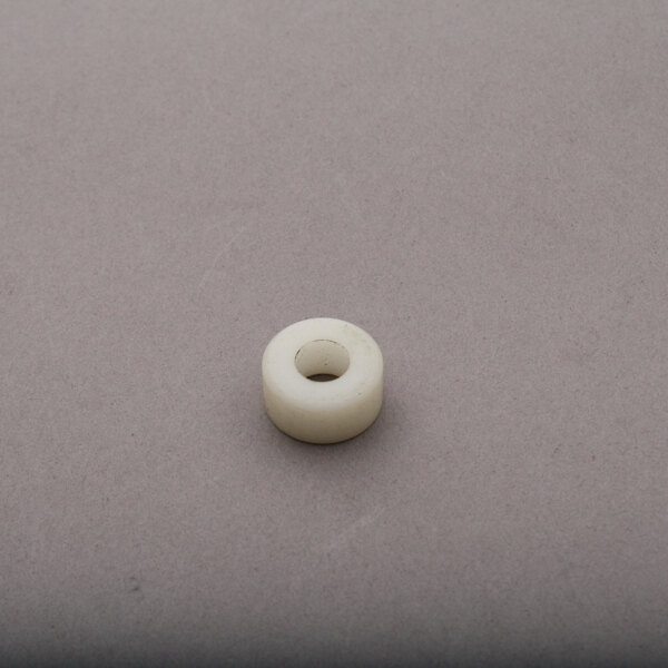 A white plastic Blakeslee 73054 spacer with a hole in the middle on a gray surface.