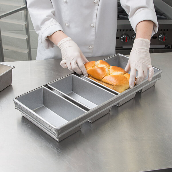 A person in a white uniform using a Chicago Metallic aluminized steel bread loaf pan to hold a loaf of bread.