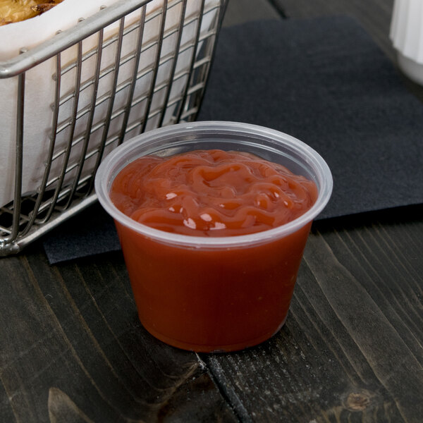 A Dart plastic souffle cup of red sauce next to a basket of food.