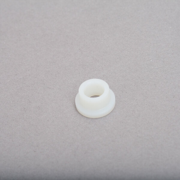 A white plastic bushing with a hole on a gray surface.