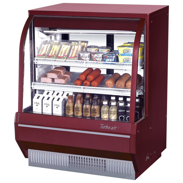 A red Turbo Air refrigerated deli case with food on shelves.