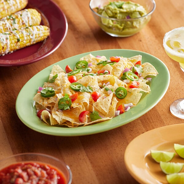 An oval Tuxton china platter with nachos, guacamole, and red sauce on a table.