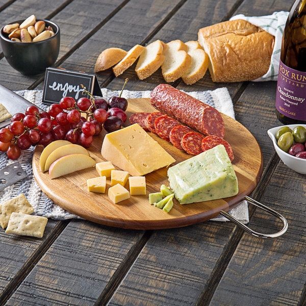 A Tablecraft acacia wood round display board with cheese, grapes, and bread on a table.