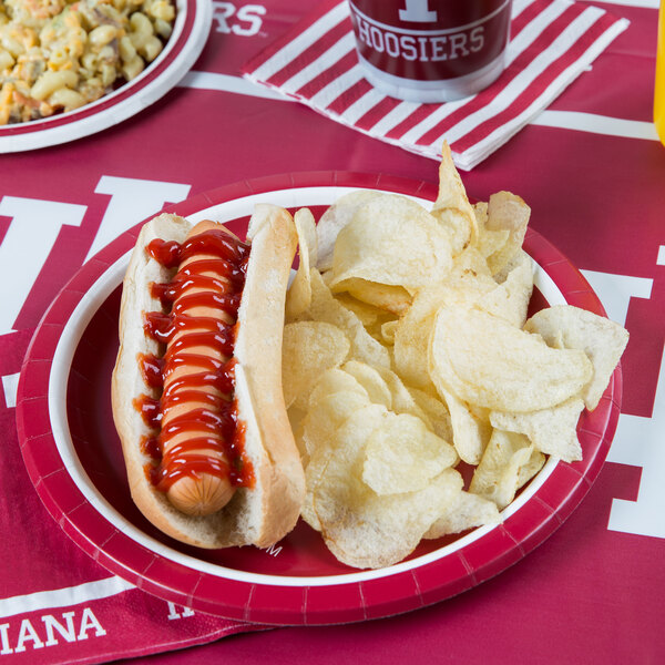 A hot dog with ketchup and chips on a Creative Converting Indiana University paper plate.