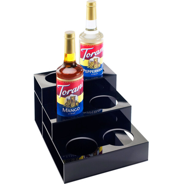 A black Cal-Mil 3 tier bottle organizer with bottles of liquid on top.