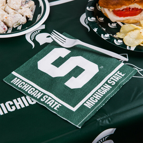 A Michigan State University Spartans 1/4 fold luncheon napkin with a logo on it next to a plate of food.