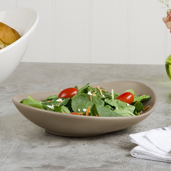 A bowl of salad with tomatoes and spinach in a Libbey Driftstone sand satin porcelain coupe plate.