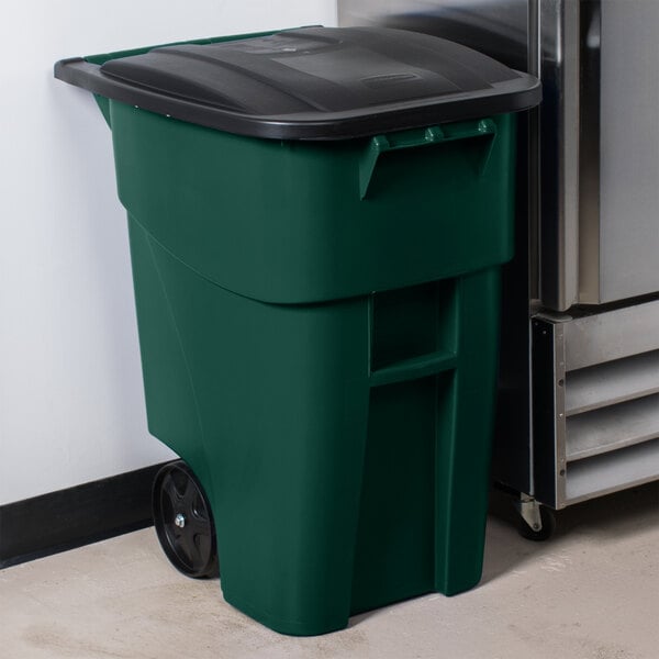 A green Rubbermaid rectangular trash can with a black lid next to a refrigerator.