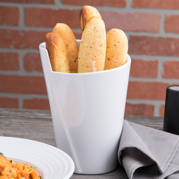 A white crock filled with bread sticks on a table next to a plate.
