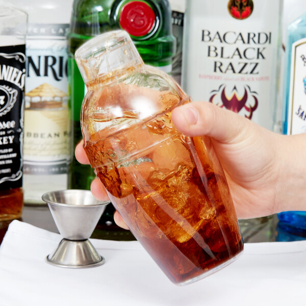 A hand using a Fineline clear plastic shaker to make a cocktail with ice.
