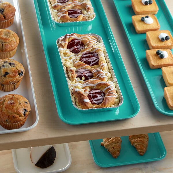 A green Cambro market tray of pastries and muffins on a bakery display table.