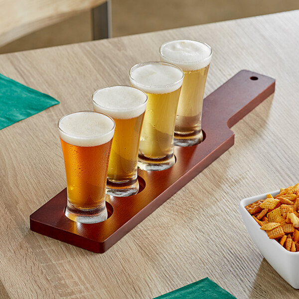 An Acopa mahogany flight paddle with flared pilsner tasting glasses of beer on a wood table.