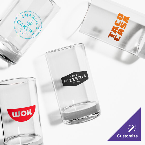 A set of four clear customizable juice or tasting glasses, each featuring a different printed logo or design.